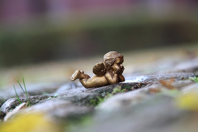 Mitfühlend leben: Skulptur: golder nachdenklicher Engel auf Stein bei Regen