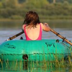 Junge Frau im Badeanzug von hinten rudert allein in einem Gummiboot über den See